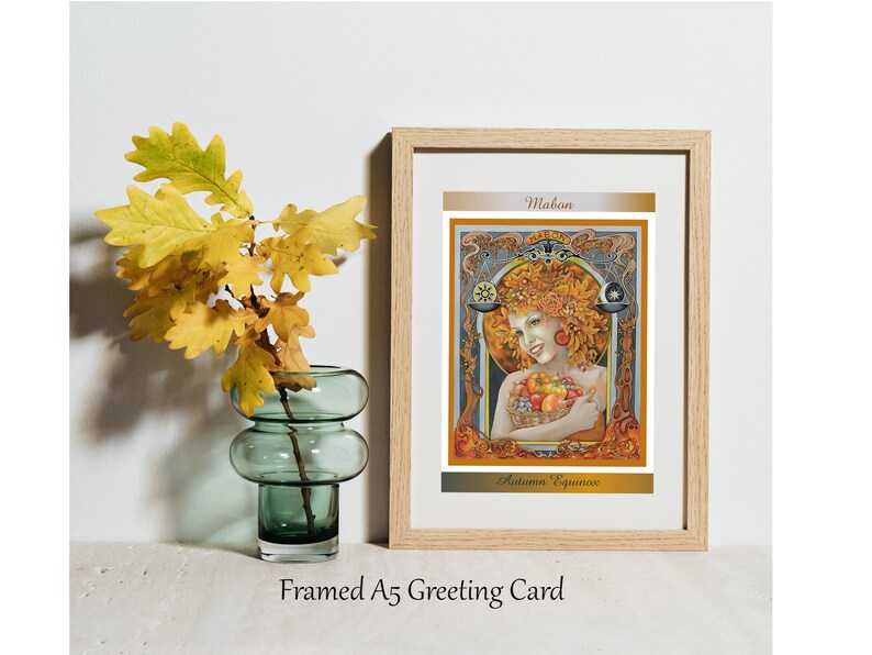 May include: Framed A5 greeting card with an art nouveau illustration of a woman surrounded by autumn leaves and fruit. The card is in a wooden frame and has the text "Mabon" and "Autumn Equinox". A green glass vase holds yellow oak leaves.