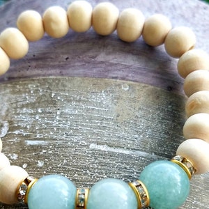 Puede incluir: Un brazalete de cuentas azul claro y blanco con detalles dorados. El brazalete está hecho con cuentas de madera y tres cuentas más grandes de color azul claro con detalles dorados.