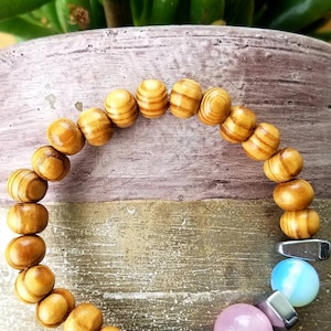 May include: A wooden beaded bracelet with three round gemstone beads in shades of pink, blue, and white. The bracelet also features silver metal spacers.