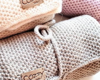 Pode incluir: Duas mantas de crochê cinzas e brancas com uma etiqueta de couro marrom que diz "Cozy Kids".