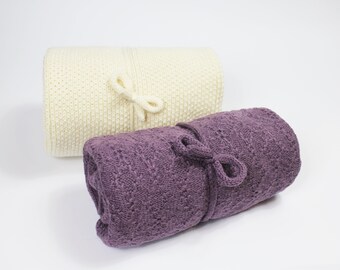 May include: Two rolled up knitted blankets, one white and one purple, with a tied bow on each.