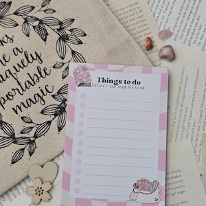 Op de afbeelding: Een roze en witte checklist met de tekst "Things to do before I can read my book" bovenaan. De checklist heeft een roze en wit gestreept patroon en een kleine illustratie van een boekentas met boeken erin.