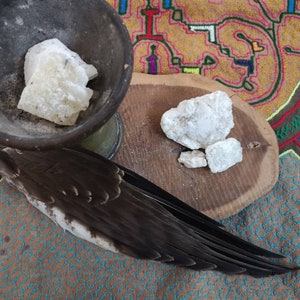 Puede incluir: Primer plano de una sustancia blanca y cristalina en un pequeño cuenco de madera. La sustancia está rodeada de una pluma de pájaro marrón. El cuenco está sobre una tela colorida.