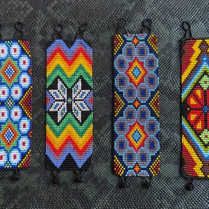 May include: Seven colorful beaded bracelets with geometric patterns. The bracelets are made with small, colorful beads and have a black string closure.