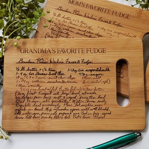 May include: Two wooden cutting boards with handwritten recipes for "Mom's Favorite Fudge" and "Grandma's Favorite Fudge". The recipes include ingredients like butter, sugar, chocolate chips, and marshmallows.