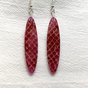 May include: A pair of dangle earrings with a pink and white snakeskin pattern. The earrings are oval shaped and have silver hooks.