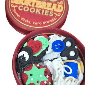 May include: A red tin of "Shortbread Cookies" with a lid featuring smiling cookie illustrations. Inside, various sewing-themed decorations are visible, including buttons, thread, and a strawberry-shaped design. The text "Sweet clicks, zero crumbs" is also present.