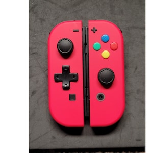 May include: A bright red Nintendo Switch Joy-Con controller with black buttons. The controller is in the open position, showing the two halves.