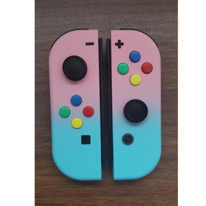 May include: A pair of pink and blue Nintendo Switch Joy-Con controllers with colorful buttons. The left Joy-Con has a black analog stick and the right Joy-Con has a black analog stick and a black button.