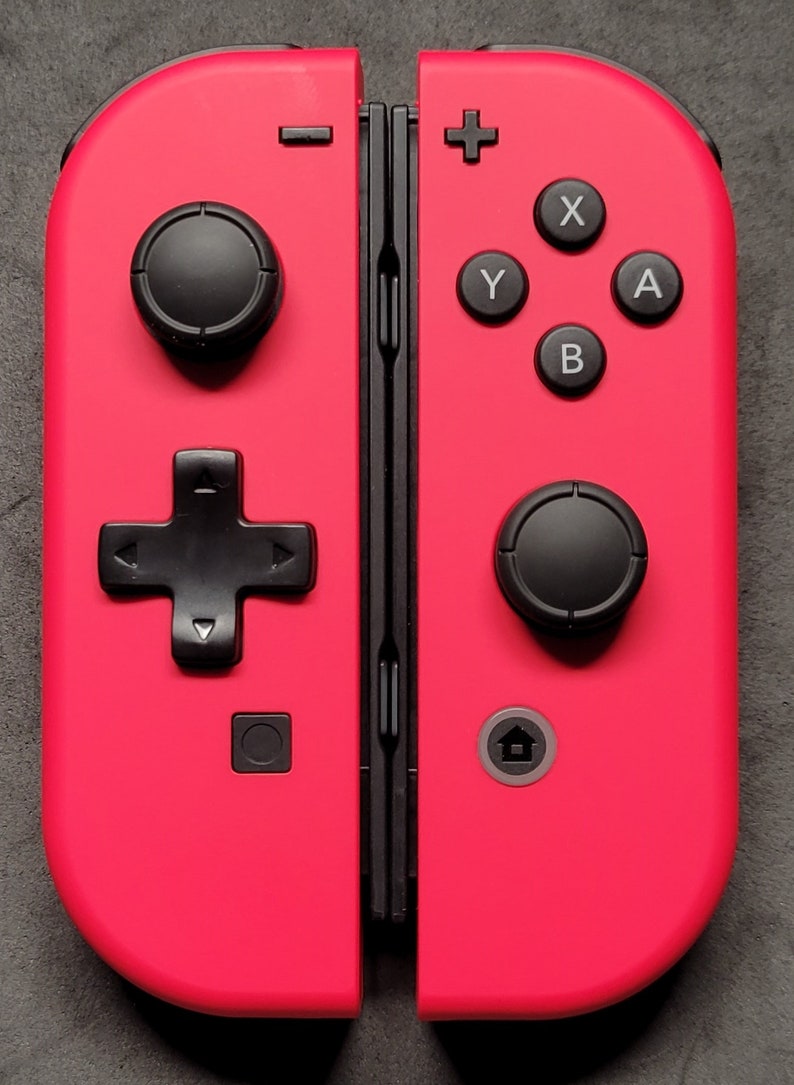 May include: A bright pink Nintendo Switch Joy-Con controller with black buttons and a black d-pad. The controller has a home button, a capture button, and a minus button.
