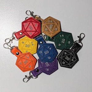 May include: A set of eight colorful leather dice charms with a 20-sided design. Each charm features white embroidery with the numbers 2, 8, 14, and 20. The charms are attached to key rings.
