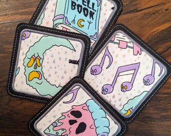 Könnte beinhalten: Vier quadratische Stoffpatches mit weißem Hintergrund und bunten Designs. Die Patches zeigen ein Buch mit dem Text "SPELL BOOK", einen Halbmond mit einem Geistergesicht, Musiknoten mit Schädeln und ein Stück Pizza mit einem Schädelgesicht.