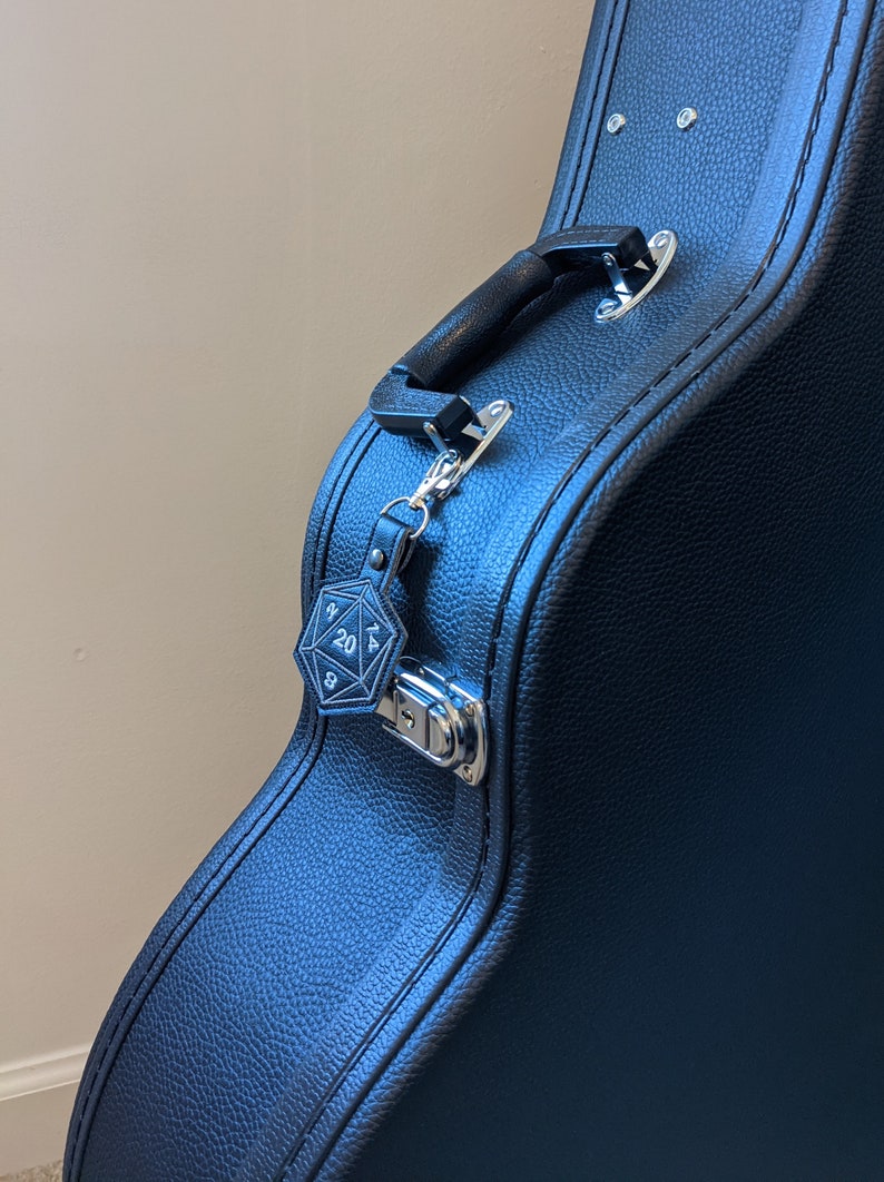 The black vinyl D20 keychain clipped onto a guitar case.