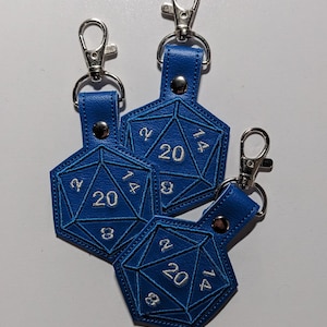 The bright blue vinyl variant of the D20 embroidered keychain.  The cutout design is shaped like a twenty-sided die, with silver thread used for the embroidered numbers, and a matching blue thread used for dice details.