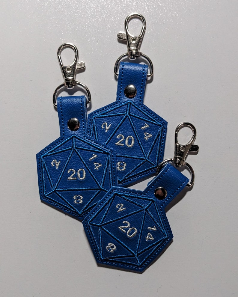 The bright blue vinyl variant of the D20 embroidered keychain.  The cutout design is shaped like a twenty-sided die, with silver thread used for the embroidered numbers, and a matching blue thread used for dice details.