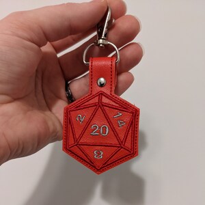 The red vinyl keychain shaped like a twenty-sided die with the numbers 2, 20, 14, and 8 visible. The keychain has a silver metal clip at the top.