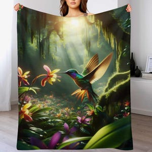 May include: A plush blanket featuring a vibrant illustration of a hummingbird in a lush jungle setting. The design showcases a colorful hummingbird with iridescent feathers, flowers, and dense foliage, bathed in sunlight. The blanket is a soft, cozy home decor item.
