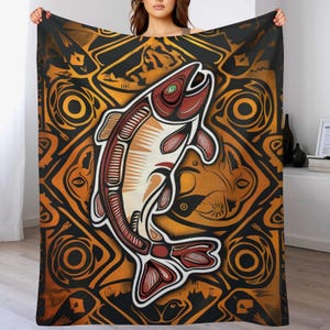 May include: A decorative blanket featuring a stylized salmon design in shades of red, cream, and brown. The fish is set against a geometric pattern in black and gold. The blanket is a cozy home decor item.