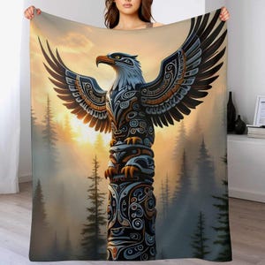 May include: A blanket featuring a detailed illustration of a Native American totem pole with an eagle at the top. The eagle has outstretched wings and is set against a backdrop of a forest and a sunset. The totem pole is in shades of black, brown, and blue.