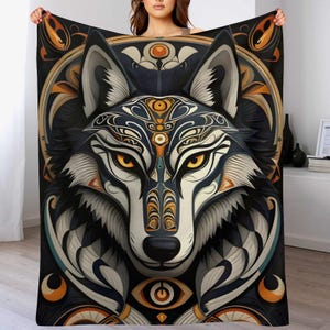 May include: A rectangular blanket with a detailed wolf head design. The design uses black, white, orange, and teal colours with intricate patterns. The wolf's eyes are yellow. The blanket is held up, displaying the full design.
