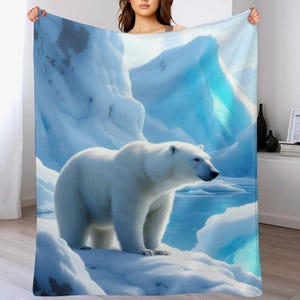 May include: A white polar bear stands on a snowy landscape in this blanket. The blanket features a detailed illustration of an arctic scene with icebergs and a blue body of water. The color palette includes shades of white and blue.