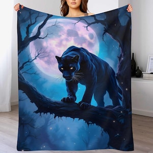 May include: A plush blanket featuring a black panther perched on a tree branch under a full moon. The artwork is set in a dark blue and purple forest scene with glowing stars and a mystical ambiance.