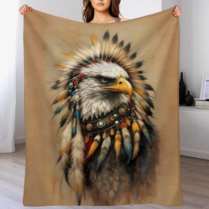 May include: A tan blanket featuring a detailed illustration of an eagle wearing a Native American headdress. The eagle has white and gray feathers, a yellow beak, and is adorned with colorful beads and feathers.