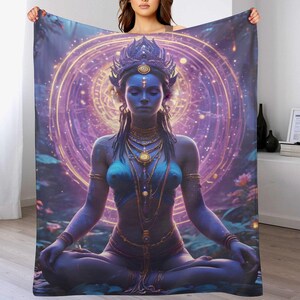 May include: A blue and purple blanket featuring a digital illustration of a meditating figure with a crown and jewelry. The figure is set against a backdrop of a glowing, circular design. The blanket is held up by a person.
