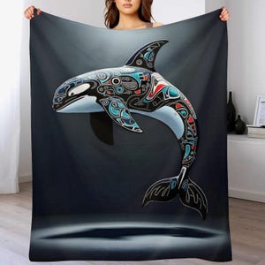 May include: A large, dark blanket featuring a stylized orca whale design. The whale is depicted in black, white, red, and teal, with intricate patterns. The background is a gradient of dark blue and gray.