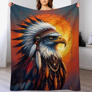 May include: A blanket featuring a detailed illustration of an eagle wearing a Native American headdress. The eagle is set against a vibrant orange and yellow background, with intricate feather and bead details. The blanket is a soft, cozy home decor item.