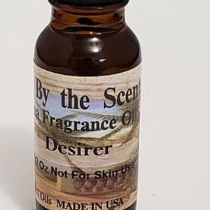 May include: A small brown glass bottle with a black cap. The label reads "By the Scent", "Fragrance Oil", "Desirer", "2 oz Not For Skin Use", and "Oils MADE IN USA".
