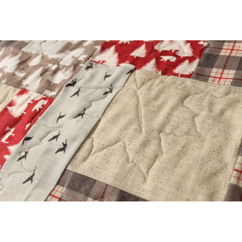 May include: A close-up of a quilt with a variety of fabrics and patterns. The quilt is made up of squares, each with a different design. The squares are sewn together to create a larger pattern. The quilt is made of a variety of fabrics, including plaid, floral, and geometric patterns. The quilt is a light brown color with hints of red and white.