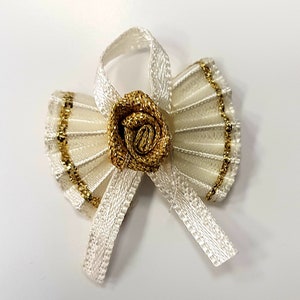 May include: Ivory-colored decorative bow with a gold rose center and gold trim. The bow features pleated fan-shaped wings and a ribbon for tying. This elegant bow is suitable for crafts, gift wrapping, or embellishments.