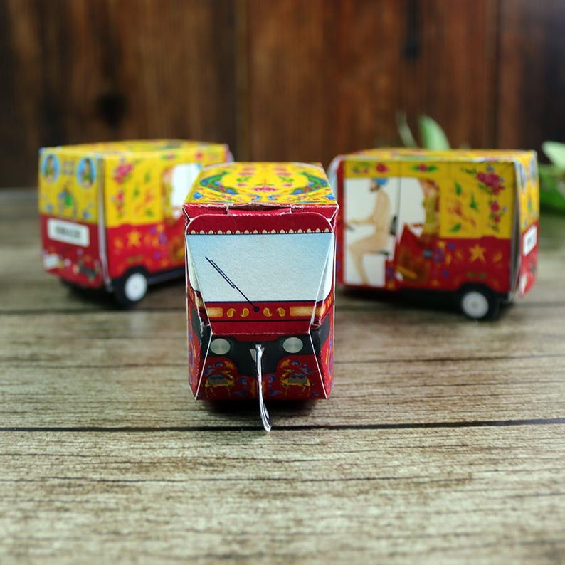 A hand holding a flat pack sheet for a red rickshaw favor box, emphasizing its convenient storage before easy folding.