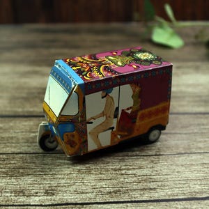 A small, brightly colored handmade rickshaw-shaped favor box, adding authentic street charm to a Desi wedding table.