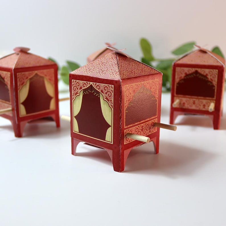 Puede incluir: Cajas decorativas de papel rojo con detalles dorados y patrones intrincados. Las cajas tienen una forma &uacute;nica, que se asemeja a peque&ntilde;as estructuras con aberturas arqueadas y clavijas de madera. El dise&ntilde;o incorpora una rica paleta de colores y detalles ornamentados.