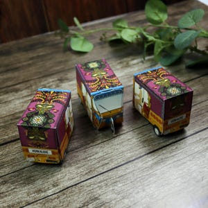 Three colorful handmade rickshaw boxes in a row, showcasing their detailed design and perfect size for wedding favors (8.5cm x 5cm x 4cm).