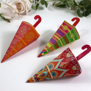 May include: Three decorative umbrella-shaped boxes with red handles. The boxes feature intricate patterns in shades of red, orange, green, blue, and purple. The boxes are arranged on a white surface, suggesting a craft or gift item.
