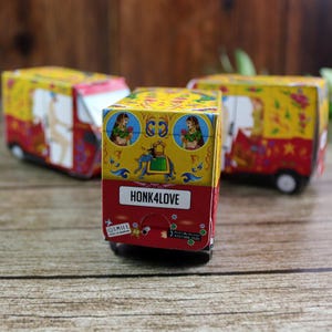 K&ouml;nnte beinhalten: Drei dekorative Miniatur-Autorikschas. Die Fahrzeuge sind &uuml;berwiegend gelb und rot, mit detaillierten Illustrationen von Figuren und floralen Mustern. Auf der Vorderseite des n&auml;chstgelegenen Rikschas steht "HONK4LOVE".