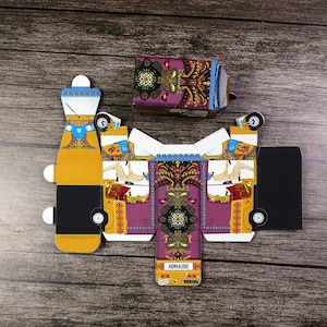 A bright yellow and purple rickshaw, flat, unassembled favor box positioned on a table, symbolizing a unique and memorable wedding favor.