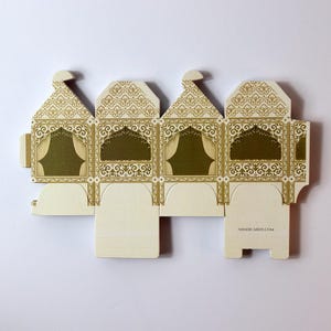 Puede incluir: Una caja de regalo desplegada de color crema con un intrincado dise&ntilde;o dorado. La caja presenta un dise&ntilde;o de arco decorativo con un borde dorado y un interior verde. El texto "SHADICARDS.COM" est&aacute; impreso en la parte inferior de la caja.