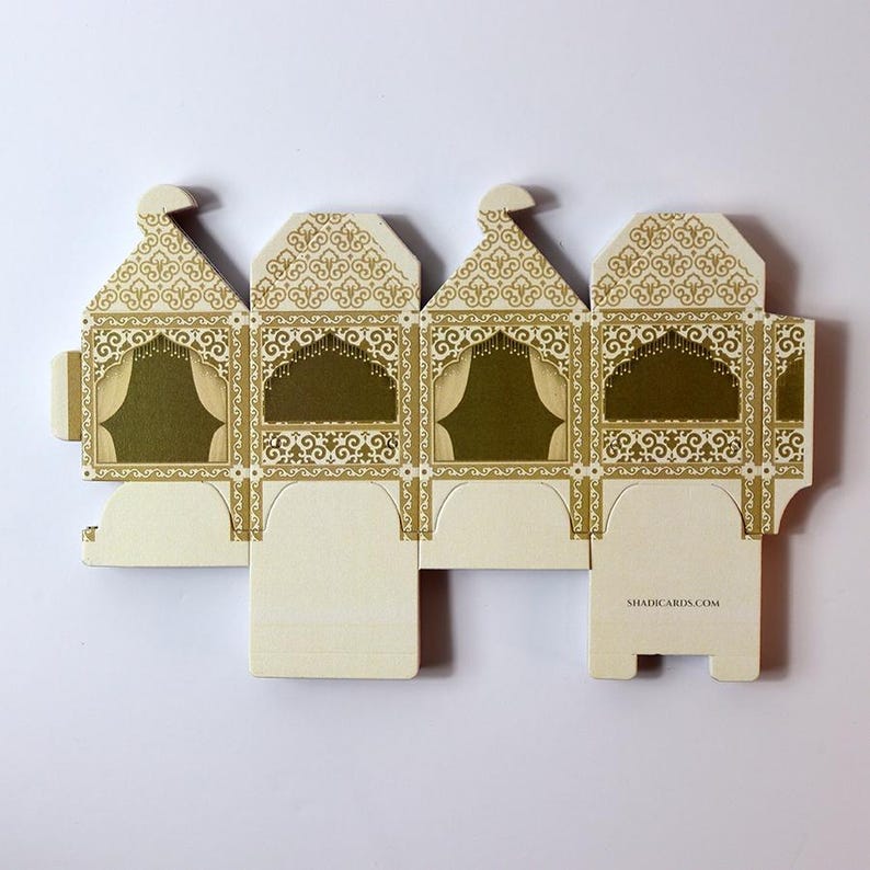Puede incluir: Una caja de regalo desplegada de color crema con un intrincado dise&ntilde;o dorado. La caja presenta un dise&ntilde;o de arco decorativo con un borde dorado y un interior verde. El texto "SHADICARDS.COM" est&aacute; impreso en la parte inferior de la caja.