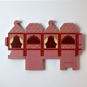 Puede incluir: Caja decorativa plana y desplegada, con una combinaci&oacute;n de colores rojo y rosa. La caja presenta un dise&ntilde;o ornamentado con ventanas arqueadas y un techo estampado. La direcci&oacute;n del sitio web, SEADICARDS.COM, est&aacute; impresa en la caja.