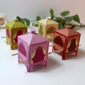 Puede incluir: Cuatro cajas de papel decorativas con forma de palanqu&iacute;n. Las cajas son de color rosa, rojo, amarillo y dorado, con patrones detallados. Las clavijas de madera est&aacute;n unidas a los lados, lo que indica que est&aacute;n dise&ntilde;adas para ser transportadas.