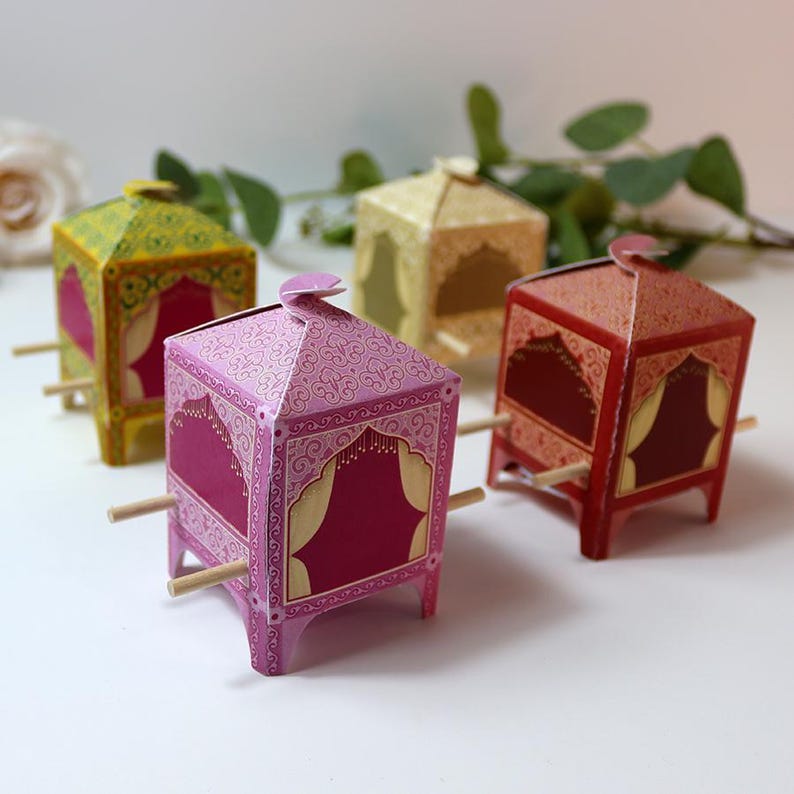 Puede incluir: Cuatro cajas de papel decorativas con forma de palanqu&iacute;n. Las cajas son de color rosa, rojo, amarillo y dorado, con patrones detallados. Las clavijas de madera est&aacute;n unidas a los lados, lo que indica que est&aacute;n dise&ntilde;adas para ser transportadas.