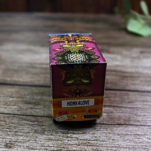 Close-up side view of a detailed rickshaw favor box, highlighting its iconic shape, traditional patterns, and wheels.