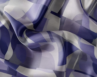 Puede incluir: Una bufanda de seda blanca con un patrón geométrico en tonos de morado y azul.