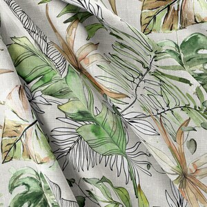 May include: A white fabric with a green and brown watercolor print of tropical leaves. The fabric is folded and has a textured surface.