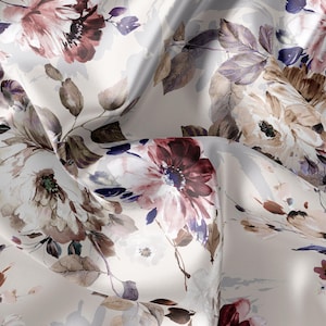 May include: A close-up of a fabric with a floral design. The pattern showcases large, watercolour-style flowers in burgundy, mauve, and cream, with purple and brown accents. The fabric appears soft and flowing, with visible folds and creases.