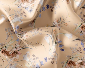 Pode incluir: Um tecido bege com estampa floral com flores brancas, rosas e marrons. O tecido tem uma textura sedosa e está drapeado de forma que o padrão é destacado.